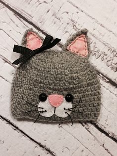 a crocheted gray cat hat with pink ears and black bow on it's head