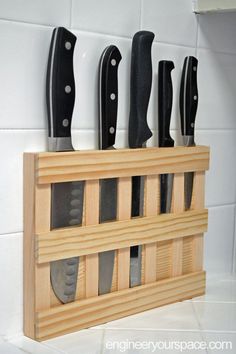 five knives mounted to a wooden holder on a tile wall with white tiles in the background