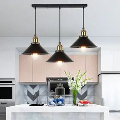 three lights hanging over a kitchen island with white counter top and black appliances in the background