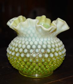 a green and white glass vase sitting on top of a wooden table next to a black wall