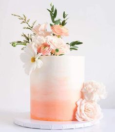 a white and pink ombreed cake with flowers on top is sitting on a plate