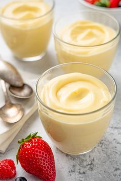 three small bowls filled with pudding next to strawberries and spoons on a table