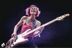 a woman with pink hair playing a bass guitar