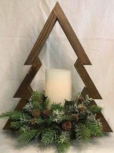 a candle is lit in front of a wooden christmas tree with greenery and pine cones