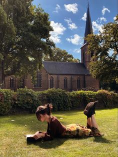 a woman laying on the grass in front of a church with a book and hat