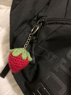 a crocheted strawberry keychain hanging from the side of a black backpack