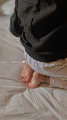 a baby standing on top of a bed next to a white blanket and pillow with the word love written on it