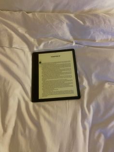 an open book sitting on top of a bed next to a white sheet covered pillow