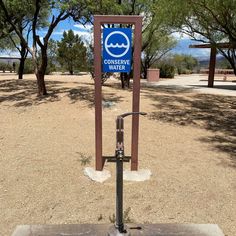 a blue sign sitting on top of a metal pole in the middle of a dirt field