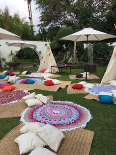 several teepees and pillows on the grass with umbrellas in the back ground