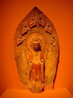 an old statue is on display in a museum setting with orange walls and red paint