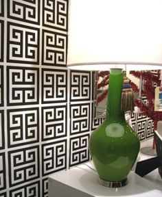 a green vase sitting on top of a white table next to a lamp with a black and white wallpaper behind it