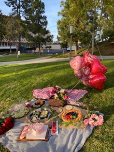 an outdoor picnic is set up on the grass with food and balloons in the background