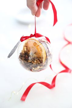 a hand is holding a glass ornament with food in it and red ribbon