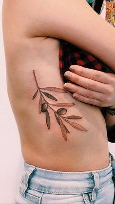 a woman's stomach with an olive branch tattoo on it