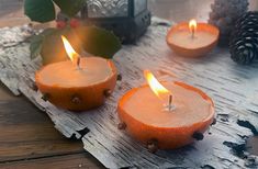 three oranges are lit on a wooden table with pine cones and candles in the background