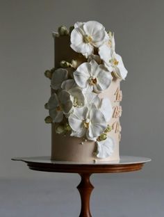 a three tiered cake with white flowers on the top and bottom, sitting on a wooden stand