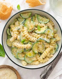 a bowl filled with pasta and cucumbers on top of a white table cloth