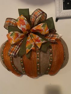 a decorative pumpkin hanging on the wall with a bow around it's neck and ribbon