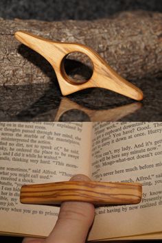 a hand holding an open book next to a wooden object