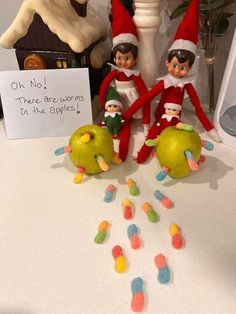 three elfs sitting on top of an apple with candy in front of them and a sign that says, oh no there are worms in the apples