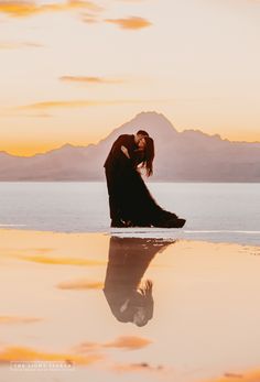 a man and woman kissing on the beach at sunset with mountains in the distance behind them