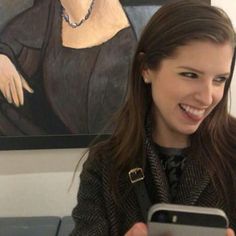 a woman smiles as she looks at her cell phone while sitting in front of a painting