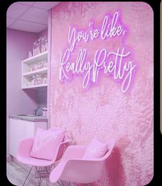 two pink chairs sitting in front of a wall with neon signs on it's side