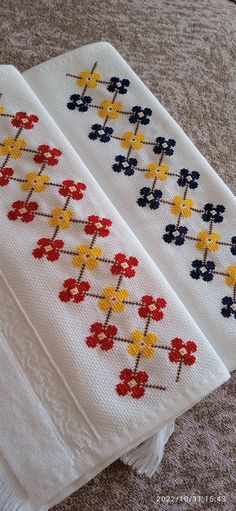 two white towels with red, yellow and blue flowers are sitting on the floor next to each other