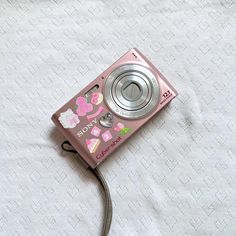 a pink camera with hello kitty stickers on it's side laying on a white sheet