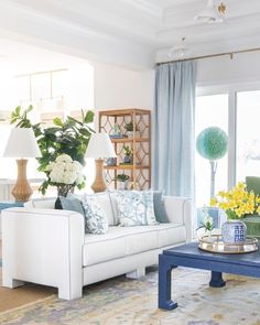 a living room filled with furniture and flowers on top of a blue table in front of a window