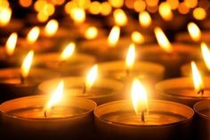 many lit candles are in rows with one candle on the side and another burning brightly