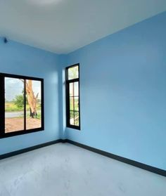 an empty room with blue walls and two windows that look out onto the field outside