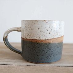 two tone coffee mug with speckles sitting on a wooden table top in front of a white wall