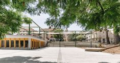 an empty parking lot surrounded by trees in front of some buildings with yellow doors and windows