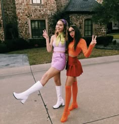 two women dressed up in costumes posing for a photo on the sidewalk with one holding her hand up