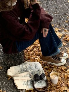 a woman sitting on the ground next to some leaves with her hand in her mouth