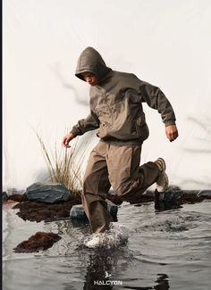 a man is jumping in the water wearing a hoodie and running through some rocks