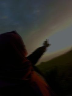 a blurry image of a person holding a cell phone up to the sky with a rainbow in the background