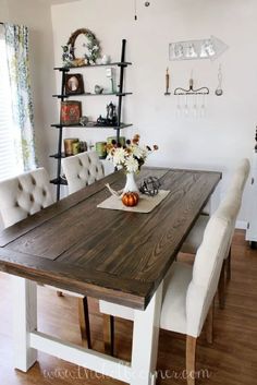 a dining room table with white chairs and an open shelf on the wall behind it