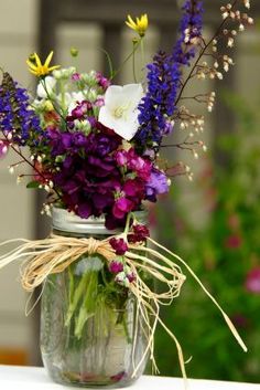 a mason jar filled with purple, white and yellow flowers on top of a table