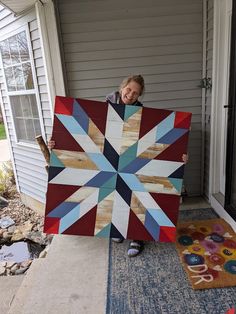 a woman holding up a large quilt on the front steps of a house with her feet in the air