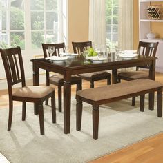 a dinning room table with chairs and a bench in front of the dining room window