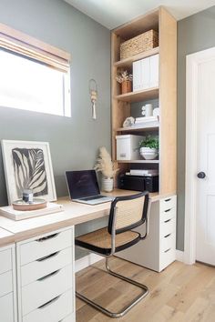 a laptop computer sitting on top of a wooden desk next to a white cabinet filled with drawers