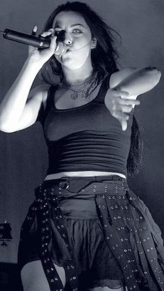 a woman in a skirt holding a microphone up to her mouth and looking into the distance