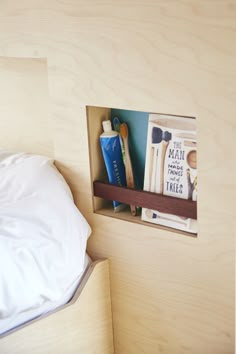 there is a book shelf in the corner of this bed that has books and toothbrushes on it