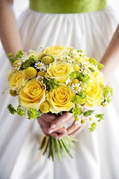 a bride holding a bouquet of yellow roses and daisies