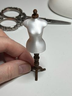 a person is holding a tiny white doll on a small metal stand with scissors in front of it