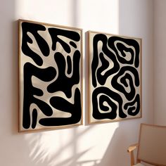 two black and white paintings hanging on a wall next to a chair in a room