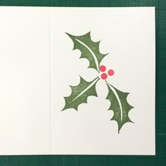 a christmas card with holly leaves and red berries on the front, in white paper